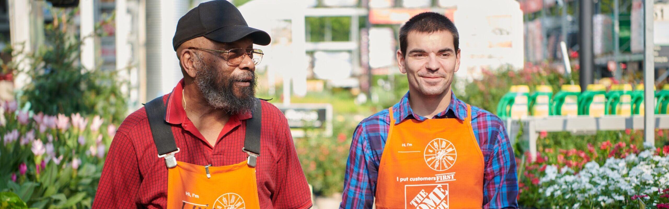 two men in Home Depot aprons among flowers in a gardening center